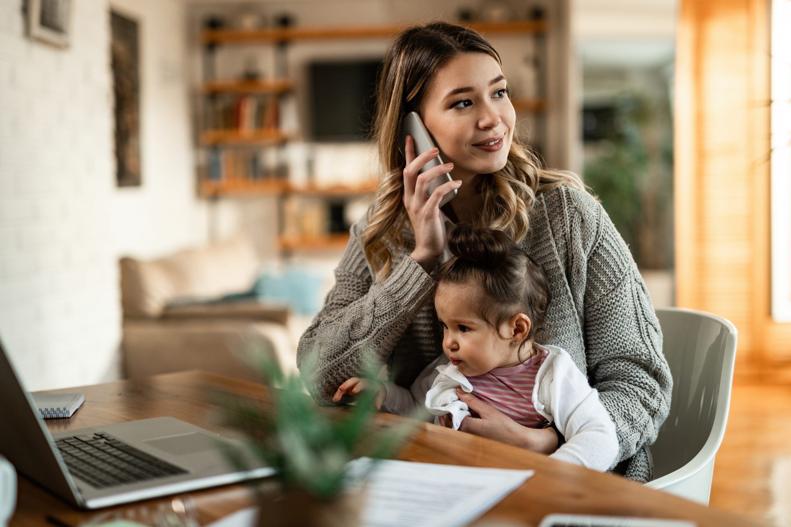 Young mother with small daughter talking on the phone at home.